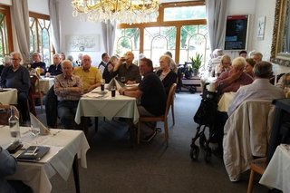 Mitglieder sitzen an Tischen im gefüllten Saal.