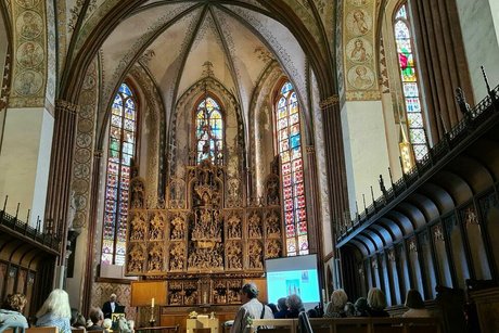 Blick ins Innere des St. Petri Doms mit seinen großen Buntglasfenstern und dem kunstvoll geschnitzten Altar im Hintergrund.
