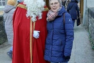 Eine Frau posiert neben einem mit roter Mitra und Mantel verkleidetem Weihnachtsmann mit Sonnenbrille.