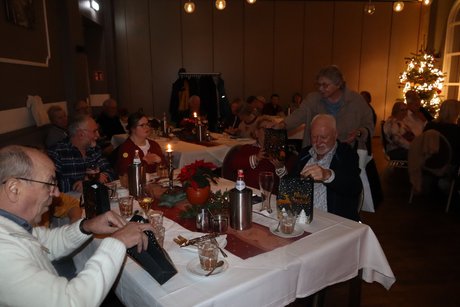Vorstandsmitglieder verteilen kleine Weihnachtst&uuml;ten an die Leute, die an gedeckten Tischen sitzen.