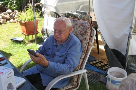 Grillnachmittag. Ein Mann Sitzt an einem Tisch und schaut auf sein Handy.