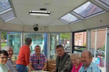 Menschen sitzen auf Holzbänken in einer zum Bus umgerüsteten Straßenbahn