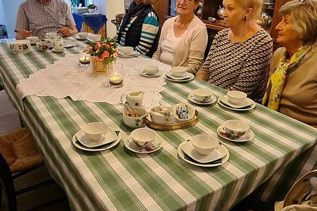 Menschen sitzen an einem Tisch zwischen Ausstellungsstücken des Teemuseums und trinken Tee aus dünnen Porzellantassen.