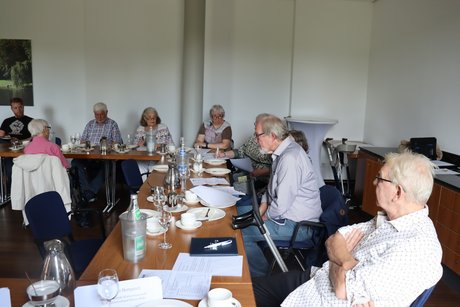 Jahreshauptversammlung 2026 Mehrere Personen sitzen an langen Tischen. Ein Mann liest etwas von einem Blatt ab.