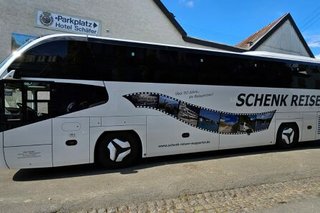 Ein großer Reisebus mit der Aufschrift Schenk Reisen steht abfahrtbereit auf einem Parkplatz.