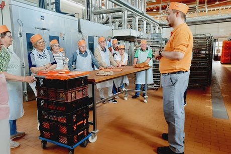 Besuch bei Bäckerei Peter. Ein Mann steht vor einer Gruppe und erklärt etwas zur Backstube.