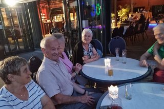 Männer und Frauen sitzen gemeinsam bei Getränken um runde Bistrotische herum und reden und lachen.