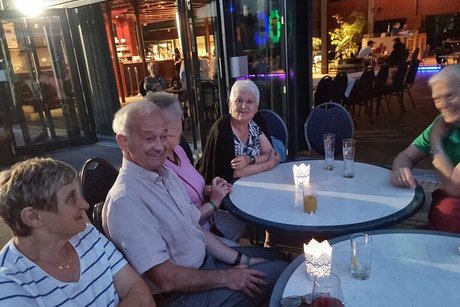 Männer und Frauen sitzen gemeinsam bei Getränken um runde Bistrotische herum und reden und lachen.