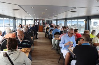 Mitglieder aus mehreren Ortsverbänden sitzen an Tischen auf dem Oberdeck des Schiffes zusammen.