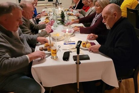 Menschen sitzen gemeinsam an einem langen Tisch beim Essen.