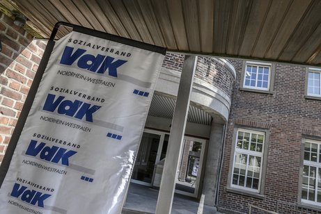 Eingangsbereich eines rotverklinkerten Geb&auml;udes mit VdK-Banner links daneben. 