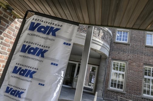 Eingangsbereich eines rotverklinkerten Geb&auml;udes mit VdK-Banner links daneben. 