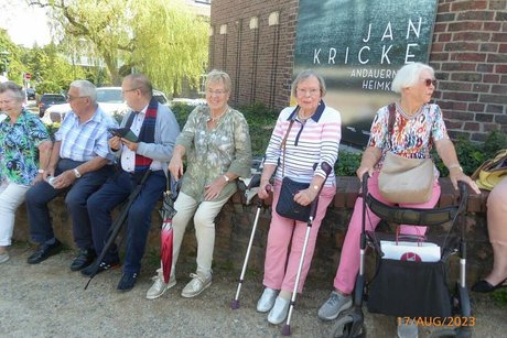 Die Reisegruppe hat auf einem Mäuerchen nebeneinander Platz genommen.