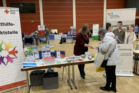 Das Bild zeigt eine Vertreterin einer Hilfsorganisation am Messestand im Gespräch mit einer Interessierten