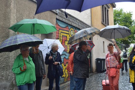 Das Bild zeigt einige Mitglieder der Gruppe, die mit Schirmen Schutz vor dem ergiebigen Regen suchten.