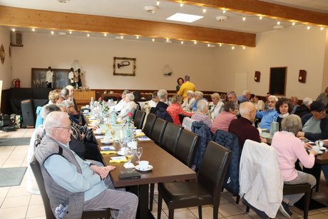 An mehreren Tischen sitzen Menschen und unterhalten sich miteinander.