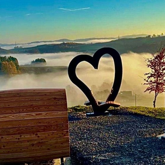 Cobbenrode, im Vordergrund ein Holzfass als Sitzgelegenheit,rechts daneben noch eine offene Schaukel f&uuml;r zwei Personen. Beide Sitzgelegenheiten bieten einen wundersch&ouml;nen ausblick, der durch ein gro&szlig;es geschwungenes Herz (ebenfalls ein Sitzplatz) &uuml;ber das nebelverhangenen Tal bei Sonnenaufgang zu sehen ist.