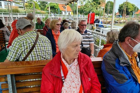 Menschen sitzen gemeinsam auf Holzbänken an Deck eines Ausflugsschiffs unter einer Markise.