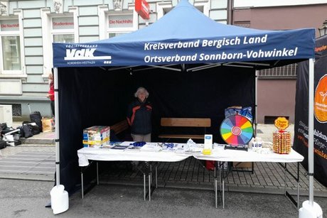 Ein blauer VdK-Pavillon mit der Aufschrift Kreisverband Bergisch Land, Ortsverband Sonnborn-Vohwinkel. Auf den Tischen Infomaterial und ein buntes, kleines Glücksrad.