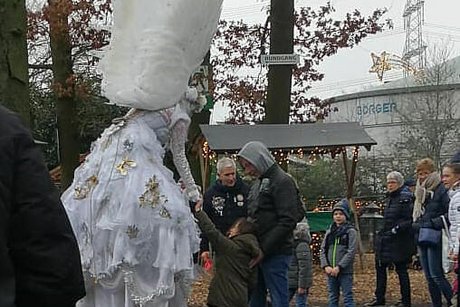 Eine als Engel verkleidete Stelzenläuferin unterhält die Besucherinnen und Besucher des Weihnachtsmarktes.