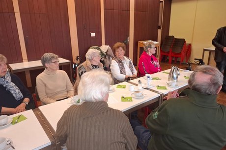 Schirmmacher Willy Schüffler hält einen Vortrag über seinen Beruf und die Geschichte des Schirms. Mitglieder sitzen an langen Tischen und hören dem Vortragenden zu.