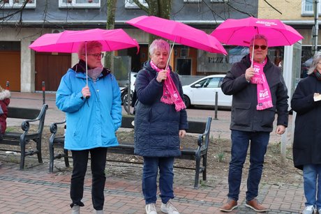 Drei Personen stehen mit bunten Schirmen in eine Menschenkette.