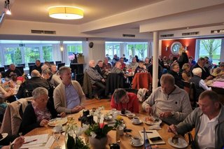 Viele Menschen sitzen an Tischen in einem Saal und essen.