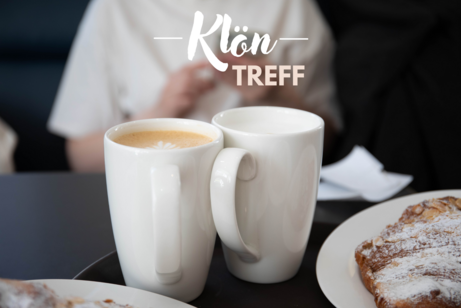 Zwei wei&szlig;e Kaffeetassen und ein Teller mit Geb&auml;ck auf einem Tisch. Dar&uuml;ber in heller Schrift: Kl&ouml;n-Treff