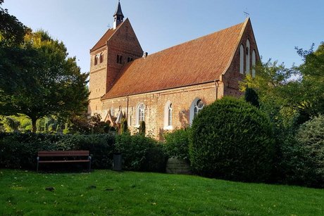 Eine Kirche steht, von der Sonne beschienen, auf einer Wiese.
