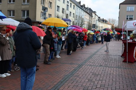 Menschen stehen mit bunten Regenschirmen nebeneinander.