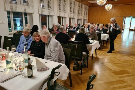 Viele Menschen sitzen gemeinsam in einem Saal an Tischen