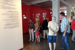 Museumsbesucher stehen vor einer Wand mit Informationen in der Dr. Oetker Ausstellung. Einige haben Kopfhörer auf den Ohren.