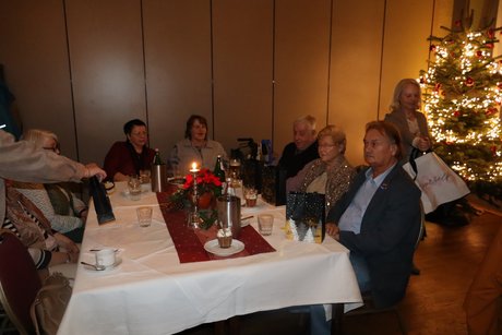 An einem Tisch sitzen mehrere Personen und bekommen kleine Weihnachtst&uuml;ten.