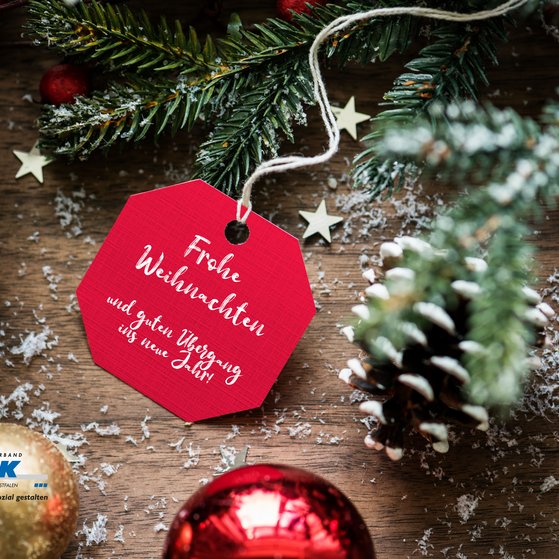 Tannenzweige, Christbaumkugeln und ein rotes Schild mit wei&szlig;er Schrift: Frohe Weihnachten.