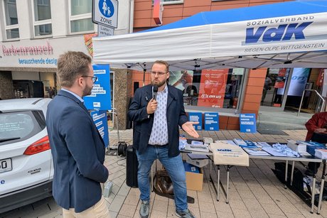 Zwei Männer im Gespräch am VdK-Stand. Einer von ihnen spricht gerade in ein Mikrofon.