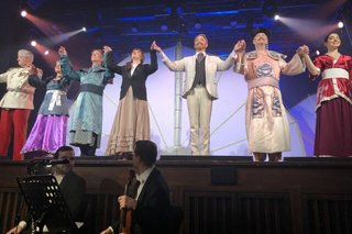 Bunt kostümierte Schauspieler der Operette "Land des Lächelns" stehen auf der Bühne, um Applaus entgegenzunehmen.