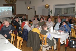 Viele Menschen sitzen in einem Saal an Tischen.