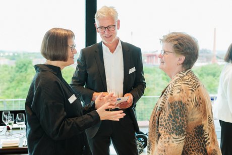 Zwei Frauen und ein Mann unterhalten sich im Stehen miteinander.