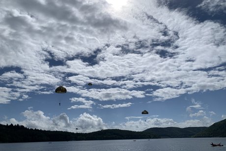 Fallschirmspringer am leicht wolkigen Himmel im Anflug auf den See