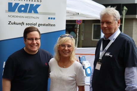 3 Personen stehen vor einem VdK Werbebanner.