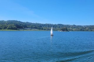 Blick über den fast spiegelglatten Edernsee. Im Hintergrund bewaldete Hügel und mitten auf dem See ein einsames Segelboot.