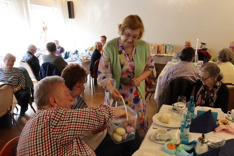Eine Frau geht mit einem Eimer mit Ostereiern von Tisch zu Tisch.
