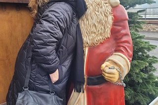 Eine Frau küsst scherzhaft eine lebensgroße Weihnachtsmannfigur, die neben einer Weihnachtsmannbude aufgestellt ist.