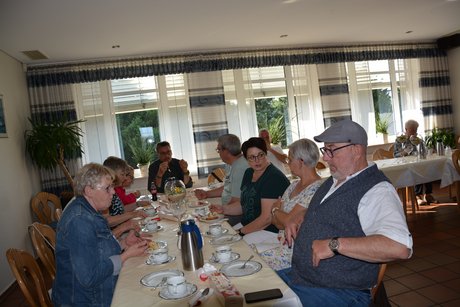 Menschen sitzen an einem Tisch trinken Kaffee und essen Kuchen