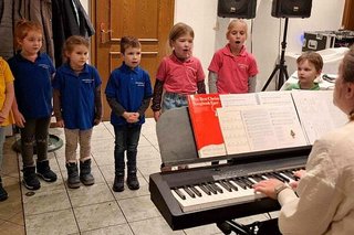 Begleitet von Keyboardmusik singen acht Kinder in bunten Shirts weihnachtliche Lieder.