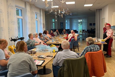 Menschen sitzen an einem langen Tisch und h&ouml;ren den beiden Referenten zu.