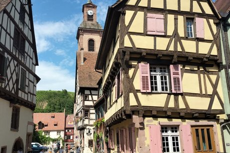 Die alte Hauptstraße in Riquewihr mit Kopfsteinpflaster und Fachwerkgebäuden; im Hintergrund überragt der Kirchturm die Häuser.