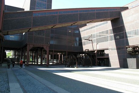 Foto auf dem Außengelände der Zeche Zollverein. Im Hintergrund erkennt man die markanten roten Ziegelmauern des Zechengebäudes und einen Fördertunnel.