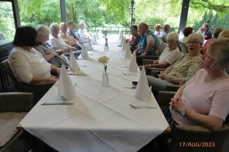 Menschen sitzen gemeinsam an einem langen, weiß eingedeckten Tisch.