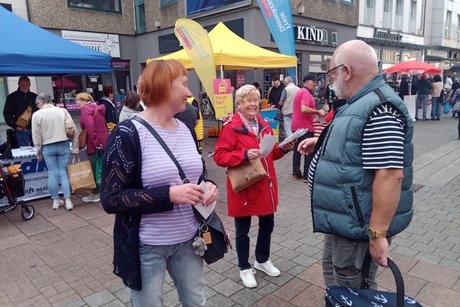 Eine Frau sprich vorbei gehende Menschen an und verteilt Info-Zettel.